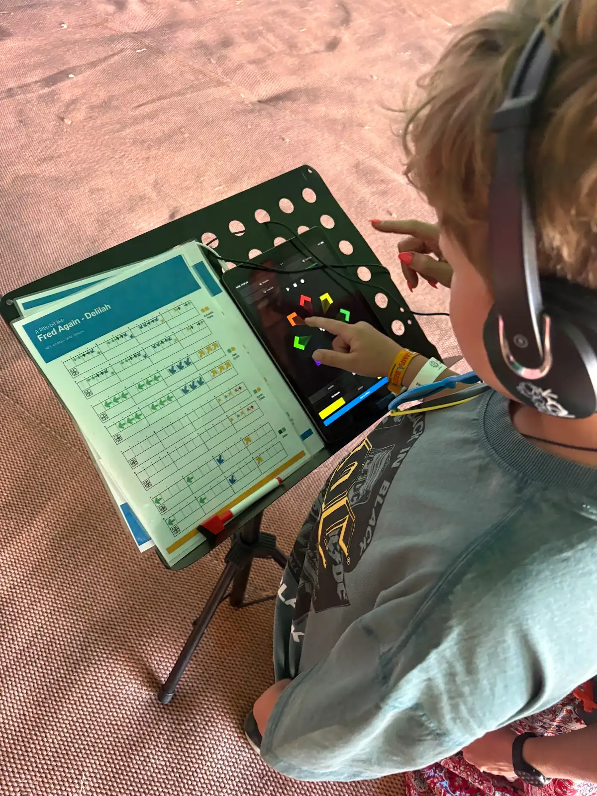 Hands playing Swipe on a tablet beside a printed musical score at a Digit Music festival session.